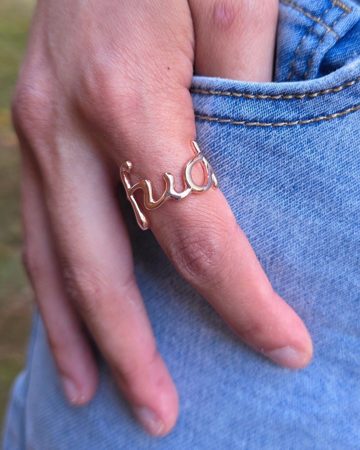 A close-up of a person's hand wearing a rose gold ring over light blue denim jeans.